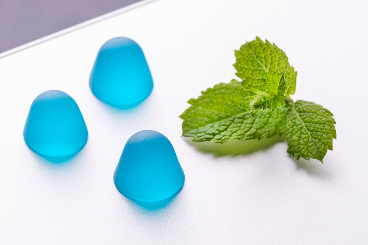 Three Dentablue gummies next to fresh mint leaves